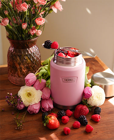 Thermos Icon food jar on a table with flowers and berries surrounding it.